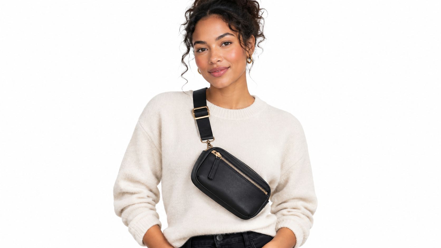 A woman wearing a beige sweater with a black crossbody belt bag over her shoulder.