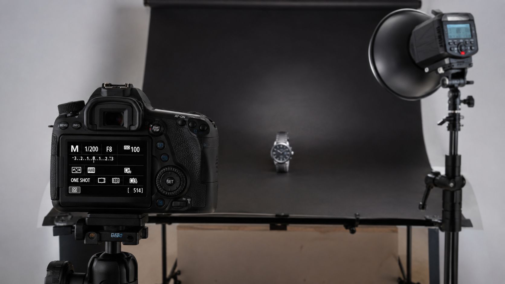 A professional DSLR camera on a tripod pointed at a watch set against a black background.