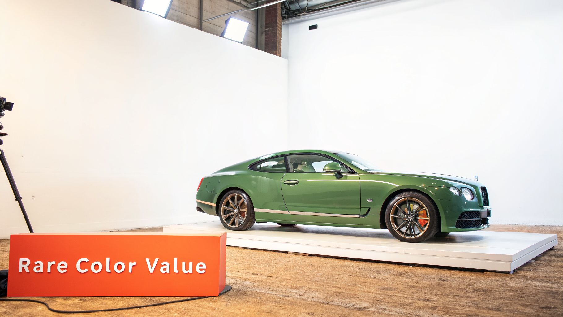 A luxurious green coupe car displayed on a white platform in a studio, with a 'Rare Color Value' sign.