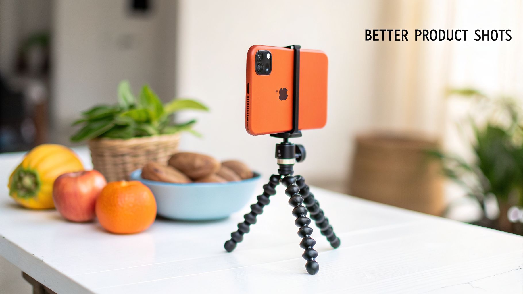 An orange iPhone on a flexible tripod capturing a scene with fruit and a plant on a white table.