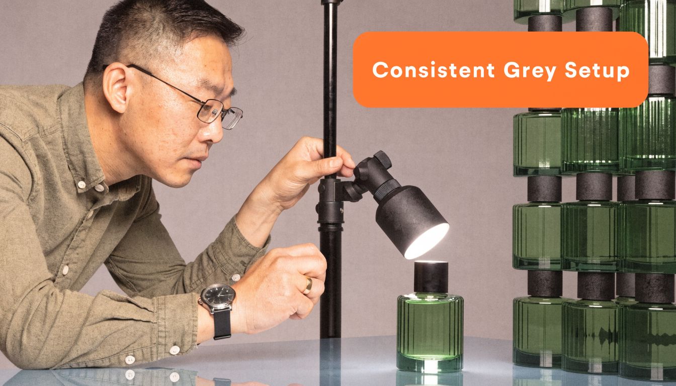 A photographer carefully adjusts lighting over a green glass perfume bottle against a neutral studio backdrop.