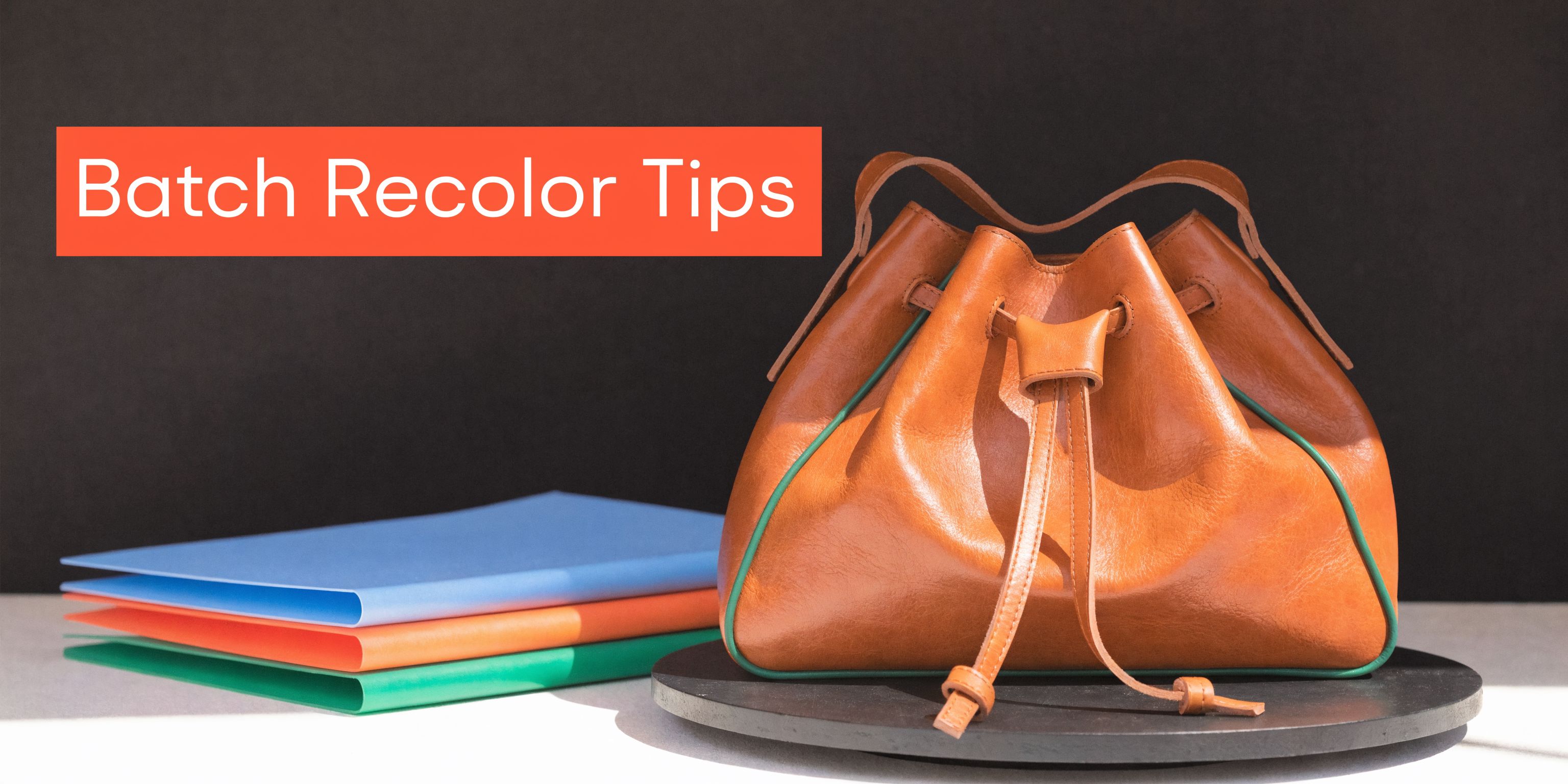 A tan leather bucket bag sitting on a black display next to a stack of colored folders.