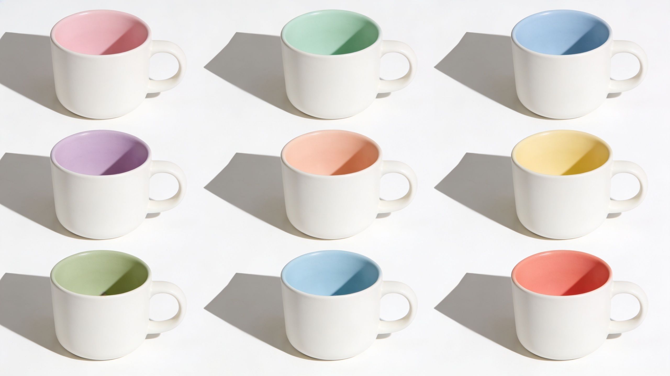 A grid of nine white ceramic mugs with different colored interiors arranged on a white background.